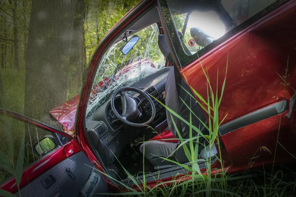 Car crashed into a tree at the bottom of an embankment with smoke rising from hood in a dreamy vignette.